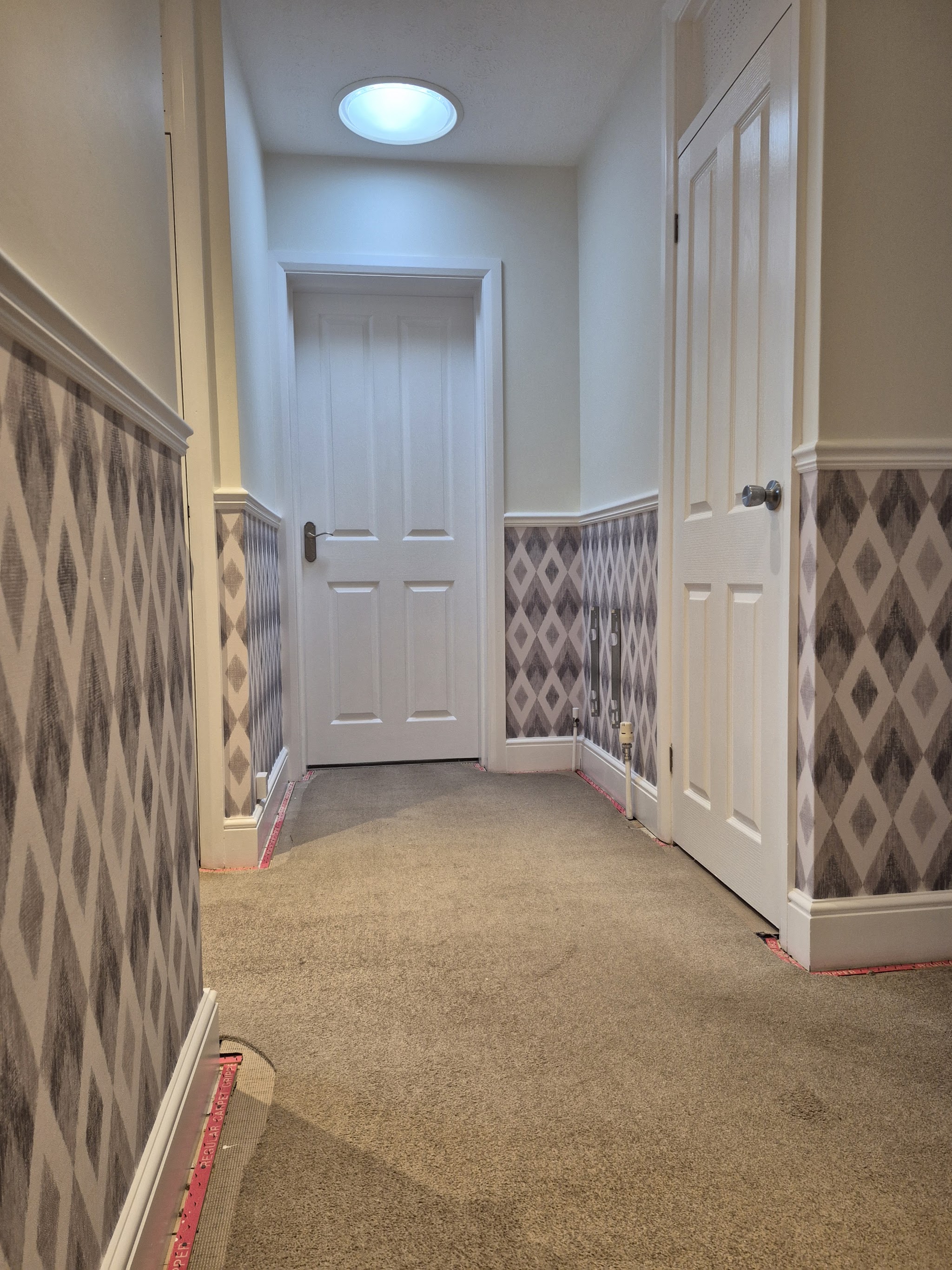 Landing with geometric wallpaper below a dado rail and white doors